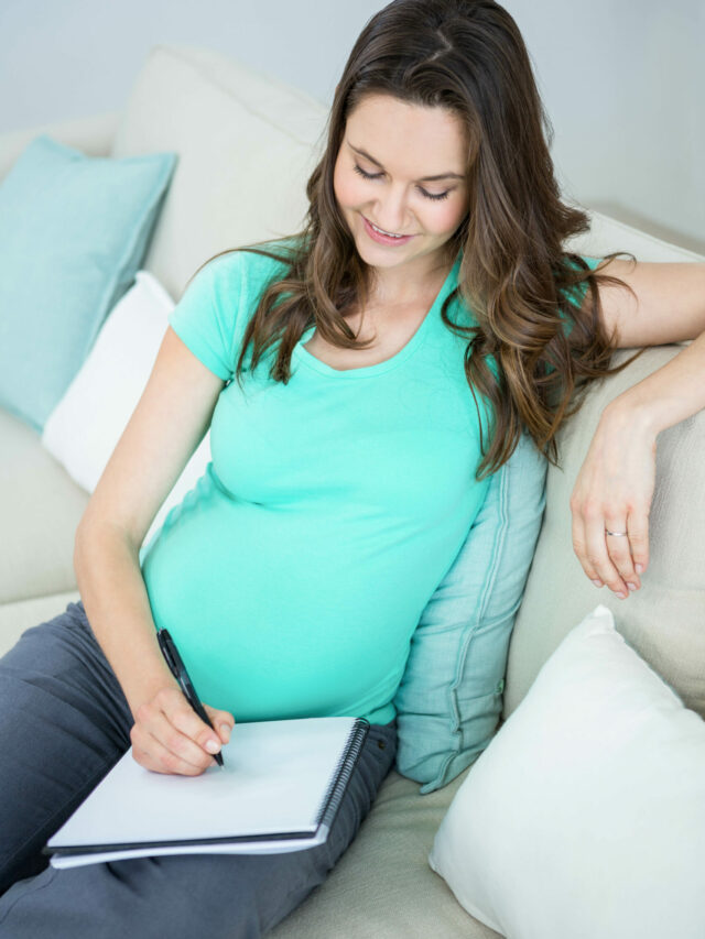 Pregnant woman writing on document on couch