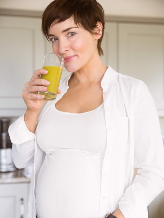 Pregnant woman drinking glass of orange juice at home in the kitchen
