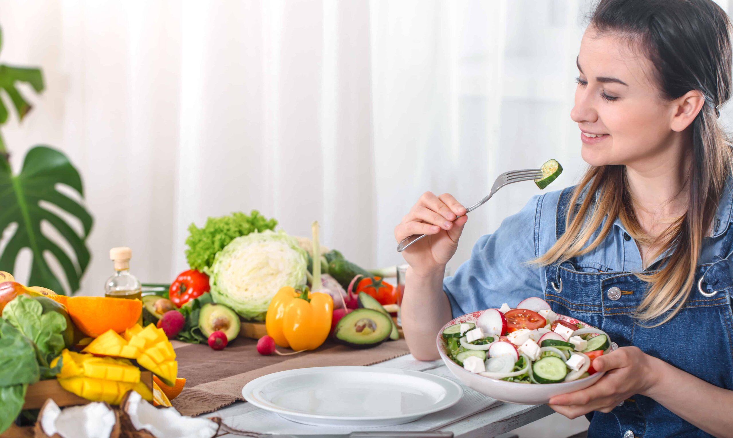 young-happy-woman-eating-salad-with-organic-vegetables-table-light-background-denim-clothes-concept-healthy-home-made-food