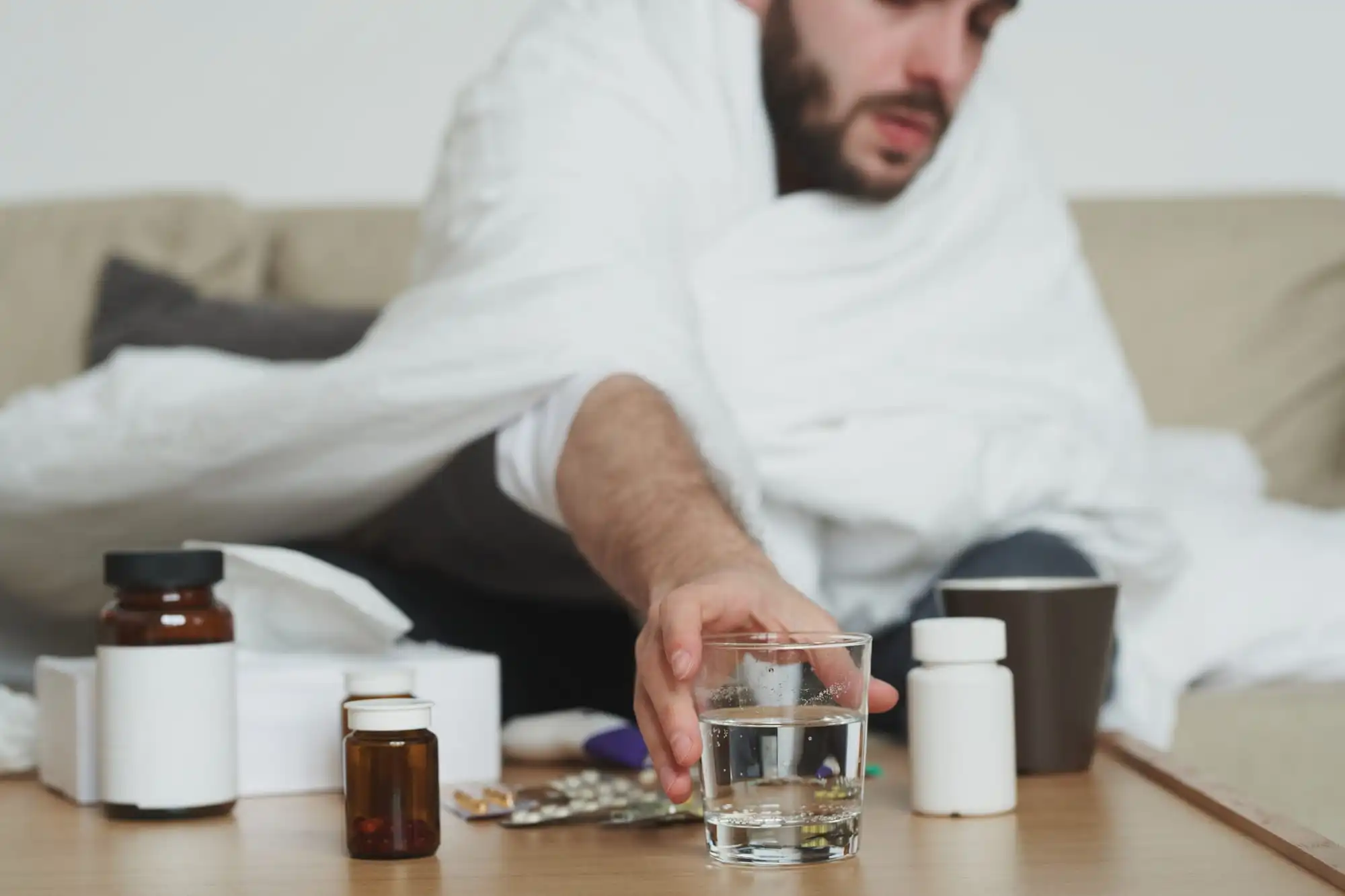 sick man covered in blanket taking medicine from table